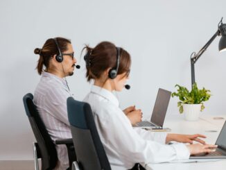 Two call centre and office agents wearing headsets working on laptops at an office desk