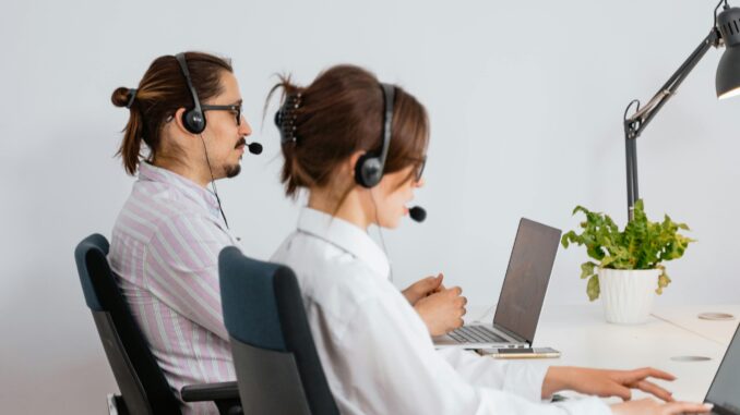 Two call centre and office agents wearing headsets working on laptops at an office desk