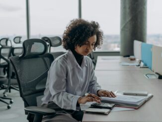 Junior office administrator working on a laptop at a desk, handling invoices and purchase orders.