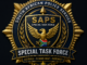 Gold and navy blue special task force style badge emblem with an eagle, shield, and decorative starburst design on a dark background.